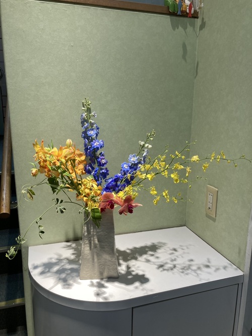 今週の院内アレンジは、爽やかなデルフィニュームと明るいオンシジュームを中心に、モカラやアルストロメリアの鮮やかな花々、グリーンの葉物をバランスよく合わせました。初夏らしい彩りと軽やかさをお楽しみください。