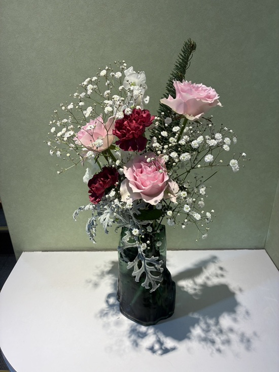 今週の院内アレンジは、モミの深い緑を基調に、やさしい色合いのバラとカーネーションを合わせました。スイートピーの軽やかさとダスティーミラーのシルバーリーフが、落ち着きの中に華やかさを添えています。