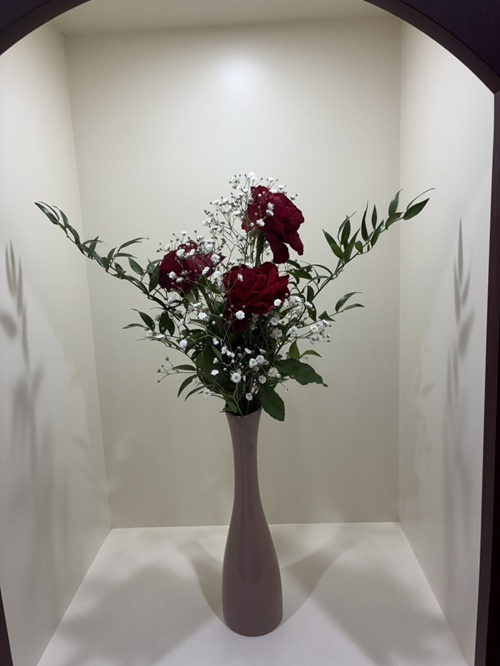 今週の院内アレンジは、深みのある赤バラを主役に、可憐なかすみ草と、すっきりとした印象のルスカス細葉を合わせた、シンプルながらも心に響くアレンジです。 情熱とやさしさが調和し、落ち着いた中にも温もりを感じる空間を演出しています。 主役となるのは、気品と華やかさを兼ね備えた赤バラ。 豊かな花びらと深い色合いが印象的で、空間に凛とした美しさと存在感をもたらします。その一輪一輪が、見る人の心に強く残る魅力を放っています。 その周囲をやさしく包み込むのがかすみ草。 小さな白い花がふんわりと広がり、赤バラの美しさを引き立てながら、全体にやわらかな空気を添えています。繊細でやさしい印象が魅力です。 そして全体を引き締めるのがルスカス細葉。 すっきりとしたラインと落ち着いたグリーンがアクセントとなり、アレンジに安定感と洗練された印象を与えています。 シンプルだからこそ際立つ花々の美しさ。 ご来院の際には、ぜひその色合いや調和を感じながら、心安らぐひとときをお過ごしください。